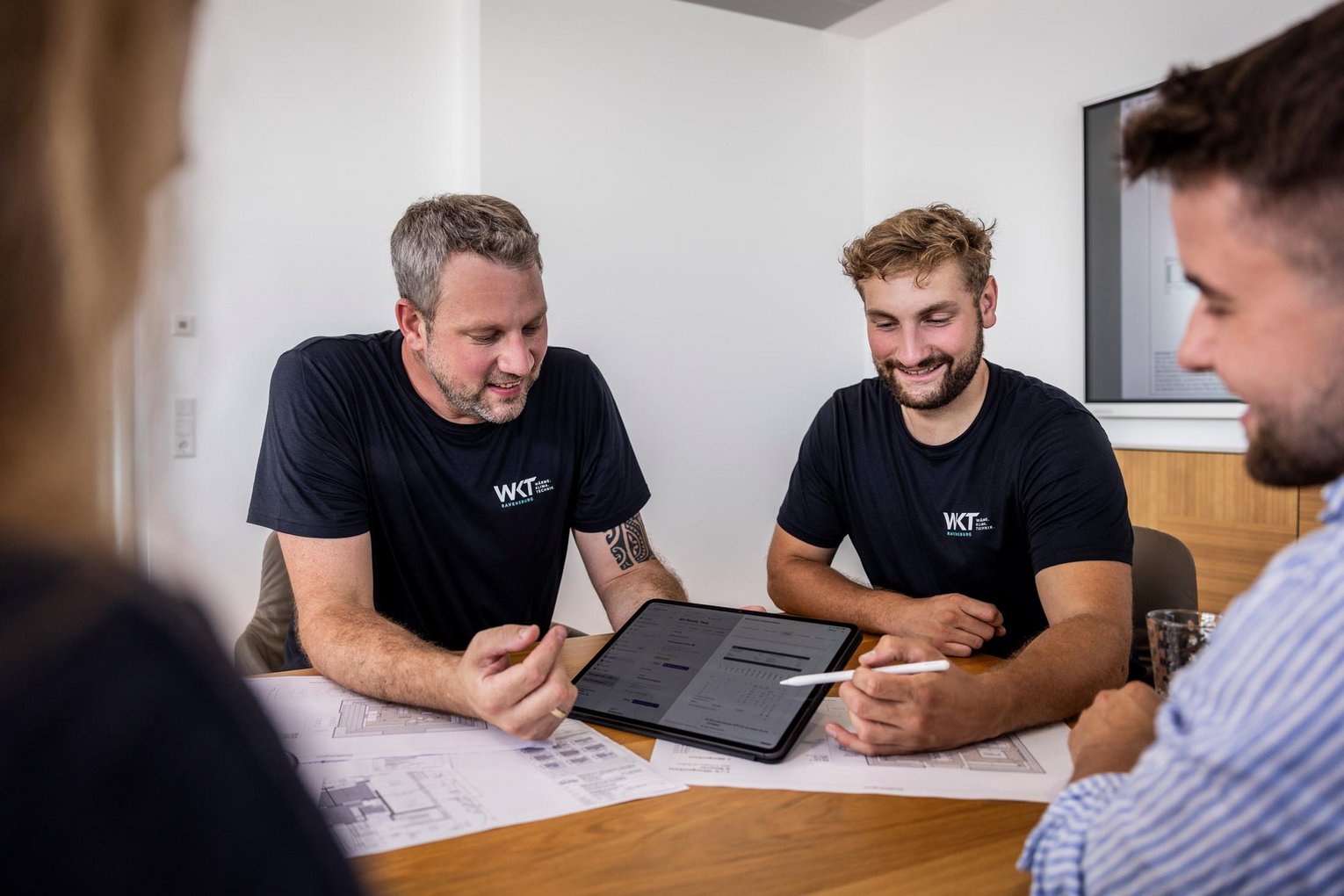 Handwerker von WKT zeigen Kunden Entwürfe und Pläne auf einem Tablet am Besprechungstisch
