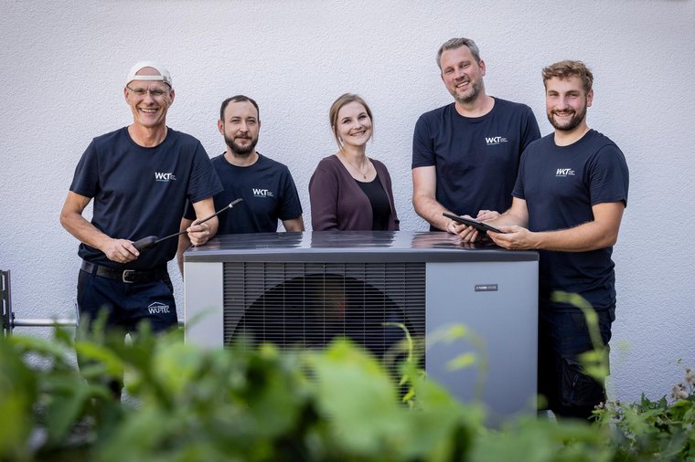 WKT-Experten für Wärmepumpen Fünf lächelnde Teammitglieder von WKT Ravensburg hinter einer montierten Wärmepumpe im Außenbereich