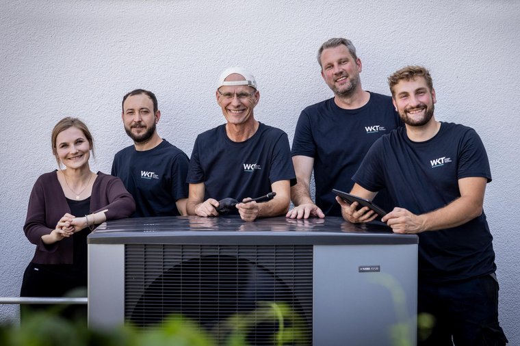 Das Team von WKT Ravensburg Fünf Mitarbeiter von WKT Ravensburg stehen gemeinsam lächelnd hinter einer Außeneinheit im Freien