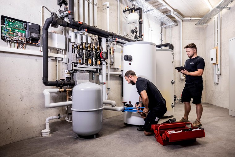 WKT-Team bei Montagearbeiten Zwei WKT-Mitarbeiter bei Montagearbeiten an einer großen Heizungsanlage im Kellerraum