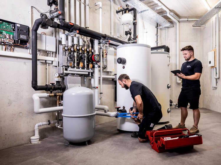 WKT-Team bei Montagearbeiten Zwei WKT-Mitarbeiter bei Montagearbeiten an einer großen Heizungsanlage im Kellerraum