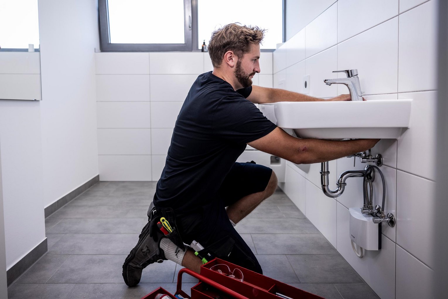 Siphon-Montage am Waschbecken WKT-Handwerker montiert in Hocke die Siphon-Anschlüsse unter einem weißen Waschbecken