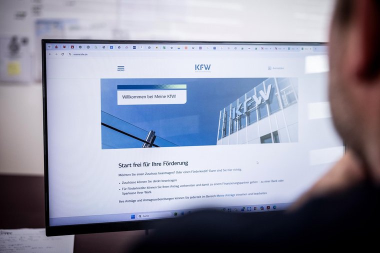 Blick über die Schulter auf einen Bildschirm mit der KfW-Förderungswebsite für Anträge
